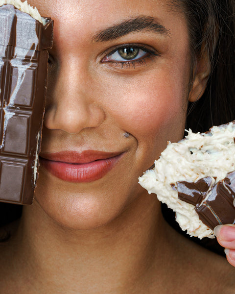 Frau mit intensivem Blick hält zwei Varianten der Dubai Schokolade – dunkle Schokoladentafel und weiße Crunchy-Mandel-Schokolade, Next Level Chocolate Trendprodukt.